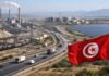 LA SEMAINE ECO | Tunisie 2026 : Fiscalité, Taux Directeur et Corridors Économiques Zone industrielle tunisienne : drapeau au premier plan, autoroute avec camions, usines et panneaux solaires, immeubles en construction en arrière-plan.