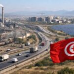 Tunisie : restructuration et gouvernance au cœur du programme de réforme des établissements publics Zone industrielle tunisienne : drapeau au premier plan, autoroute avec camions, usines et panneaux solaires, immeubles en construction en arrière-plan.