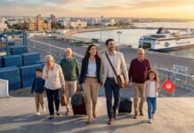 Fuite des cerveaux : Pourquoi les compétences tunisiennes envisagent-elles de quitter l’Europe ? Photographie aérienne d'une famille multigénérationnelle de la diaspora (6 personnes) débarquant joyeusement d'un ferry dans le port de Tunis (La Goulette). Au premier plan, un couple qualifié tire des valises, un grand-parent est ému, et un enfant tient un drapeau tunisien. En arrière-plan, le grand ferry 'TUNISIA LINE' et les infrastructures portuaires sont éclairés par la lumière dorée du lever du soleil.