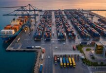 Tunisie : La BCT verrouille la stabilité, la relance attend Photographie éditoriale aérienne du port de Radès en Tunisie au lever du soleil. Des portiques de déchargement modernes, des piles de conteneurs et un navire cargo sont visibles.