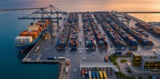 Tunisie : La BCT verrouille la stabilité, la relance attend Photographie éditoriale aérienne du port de Radès en Tunisie au lever du soleil. Des portiques de déchargement modernes, des piles de conteneurs et un navire cargo sont visibles.