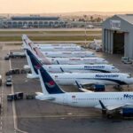 Transport Aérien : Quand Nouvelair prend de l’altitude Vue aérienne au lever du soleil sur le tarmac de l'aéroport Tunis-Carthage. On y distingue clairement une rangée d'avions de la compagnie privée Nouvelair (livrée blanche et bleue, incluant le nouvel A320neo) alignés parallèlement à une rangée d'appareils Tunisair (livrée blanche avec la gazelle rouge).