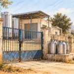 Filière laitière : cinq centres de collecte fermés à Sidi Bouzid Centre de collecte du lait fermé, portail cadenassé et bidons métalliques dans un paysage rural évoquant Sidi Bouzid